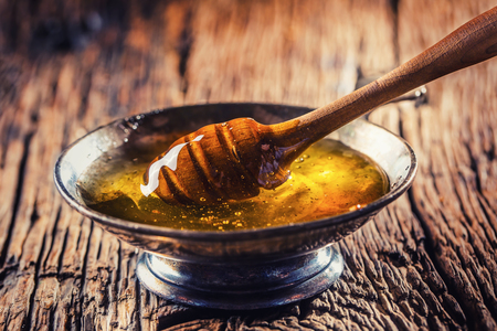 Honey. Honey and honey dipper on rustic oak table. Hot herb tea in the background.の写真素材