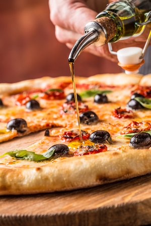 Chef and pizza. Phef pouring olive oil on  pizza in hotel or restaurant.の写真素材