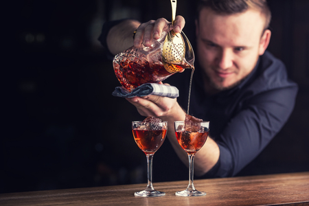 Bartender pouring cocktail alcoholic drink Manhattan. Barman in pub or restaurant  preparing a cocktail drink.の写真素材
