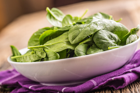 Spinach. Fresh baby spinach leaves in plate on woden table.の写真素材