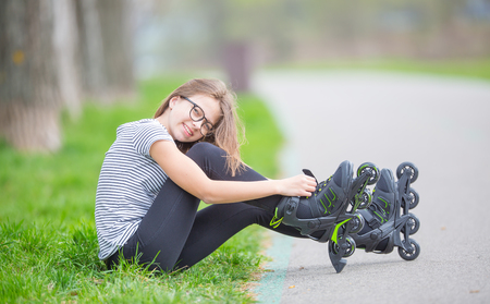 Cute young going rollerblading sitting in grass putting on inline skates.の写真素材