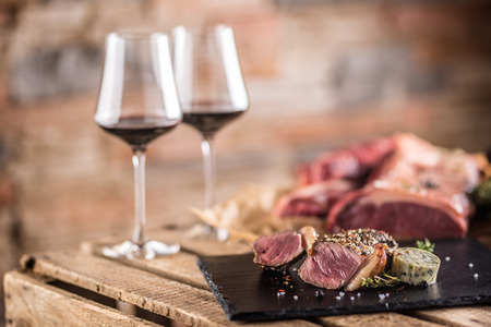 Two cups with red wine roasted and raw beef steak on slate board.の写真素材