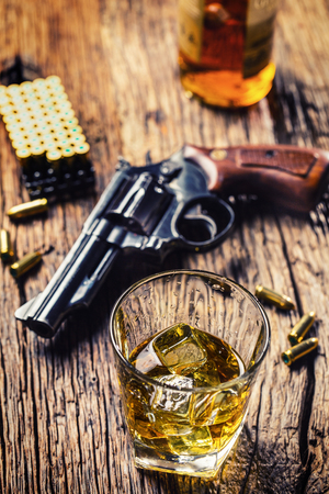 Glass of whiskey cognac or bourbon with revolver and bullets on wooden table.の写真素材