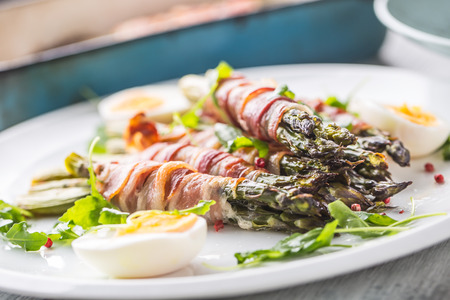 Fresh asparagus wrapped in bacon  on a white plate with arugula tomatoes and eggs.の写真素材