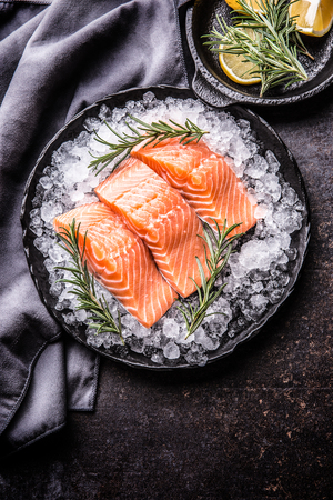 Portioned raw salmon fillets in ice on plate with lemon and rosemary.の写真素材