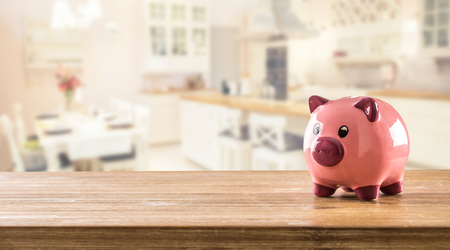 Pink piggy bank on table and blurred home kitchen in the background.の写真素材
