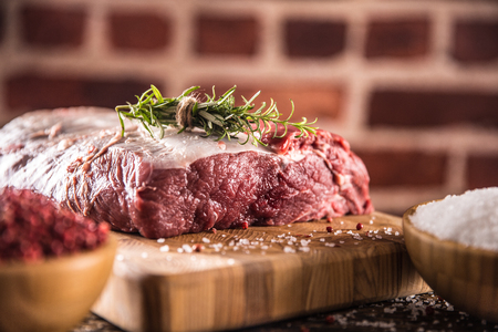 Raw beef ribe-eye steak with salt pepper and herbs on wooden butcher board.の写真素材