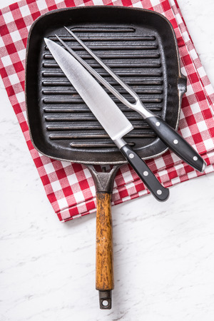 Empty grill pan on marble table with red tablecloth knife and fork - top of view.の写真素材