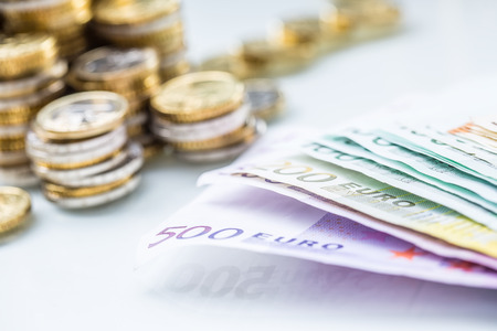 Euro banknotes and coins togetger on white table - close-up.