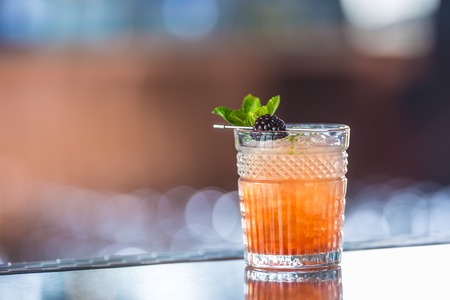 Cocktail drink bramble with black berries and mint at barcounter in night club or restaurant.