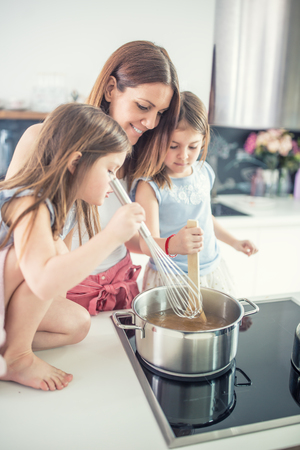 Mom with two young twins daughters in the kitchen cooking spaghetti.の写真素材