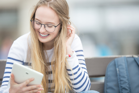 Portrait of a smiling beautiful teenage girl with dental braces. Young schoolgirl with school bag and tablet device.の写真素材