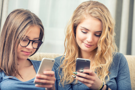 Two teen girs or sisters using smart phones in the living room.