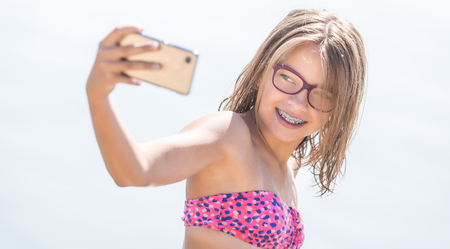 Happy young girl with dental braces making selfhie on beach in summer hot day.の写真素材