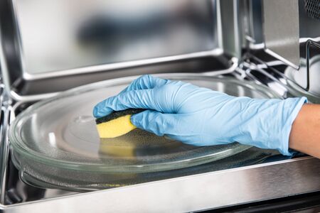 Woman hand cleaning microwave oven with sponge.