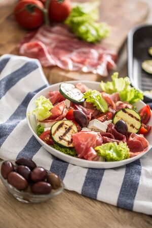 Fresh lettuce salad with grilled zucchini coppa di parma ham feta cheese olives tomatoes and olive oil.の写真素材