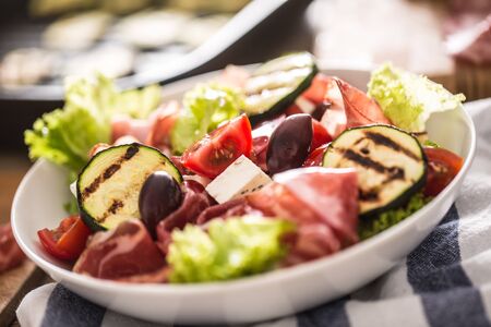 Fresh lettuce salad with grilled zucchini coppa di parma ham feta cheese olives tomatoes and olive oil.の写真素材