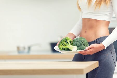 Young woman with sports figure in the kitchen holding in her hands and a plate of broccoli.の写真素材