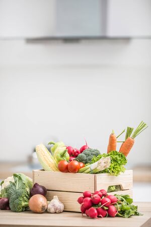 Wooden box full of fresh healthy vegetables. Broccoli carrot radish onion garlic corn on wooden kitchen table.の写真素材