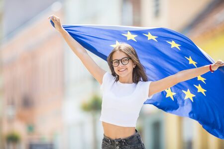 Cute happy young girl with the flag of the European Union in the streets somewhere in europe.の写真素材
