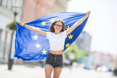 Cute happy young girl with the flag of the European Union in the streets somewhere in europe.の写真素材