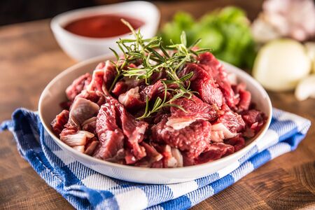 Raw beef pieces with rosemary in bowl on butcher board.の写真素材