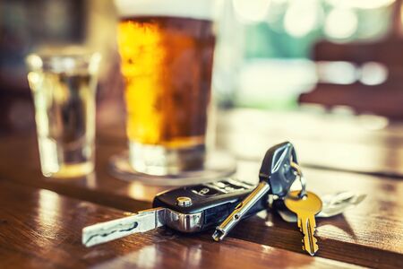 Car keys and glass of beer or distillate alcohol on table in pub or restaurant.の写真素材