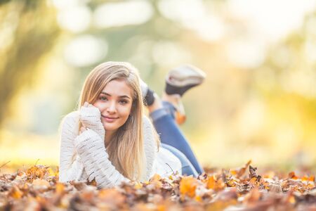 Autumn portrait of young woman lying on maple leaves in park.