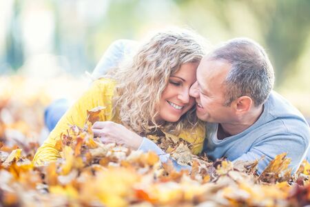 Happy senior couple lying in autumn maple leaves.の写真素材