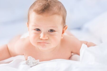 Portrait of cute toddler boy lying on bed. Newborn child in bedroom. Baby lies on his tummy and...