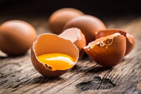 Broken chicken eggs with yolk on wooden table.