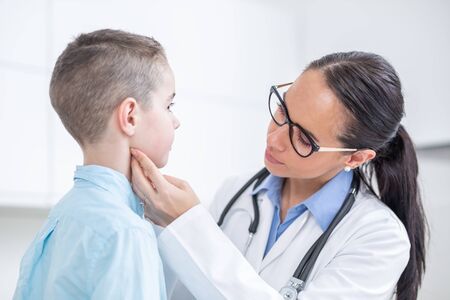 Doctor woman examining tonsils of young boy in medical office.の写真素材
