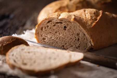 Freshly baked bread slice and loaf detail with a knife placed beside on a rustic background.