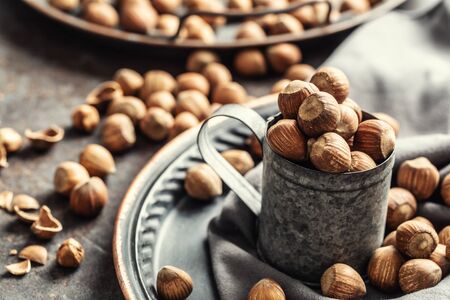 Hazelnuts and their cracked shells on a vintage dark metallic background, in a metallic cup and on a tray with a cloth.の写真素材