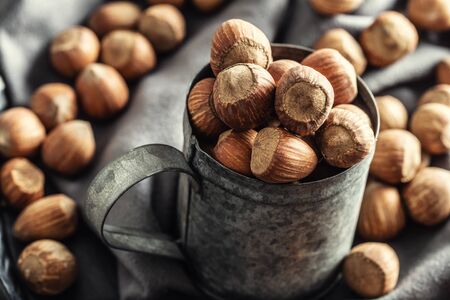 Close up of a vintage metallic mug full of hazelnuts with more nuts on a textile table cloth around it.の写真素材