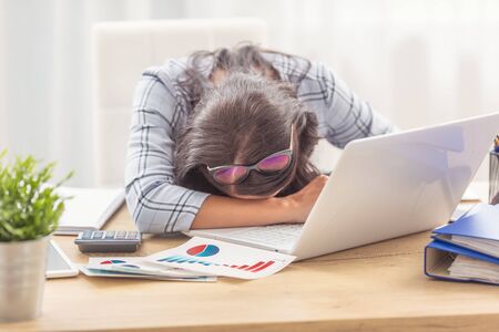 Woman fallen asleep on her working desk with business graphs and a notebook in front of her.