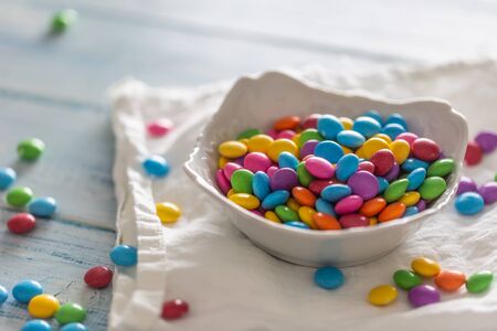 Smarties put in a white porcelain bowl and scattered around on a white clothe and a table.の写真素材