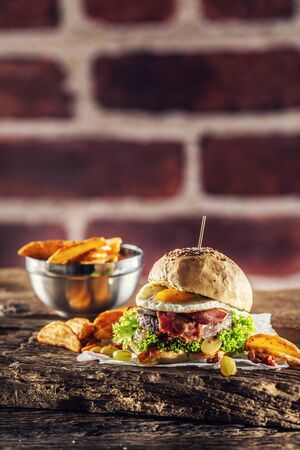 Beef burger with fried egg, bacon, lettuce, potato wedges and grapes on a rustic wood.の写真素材