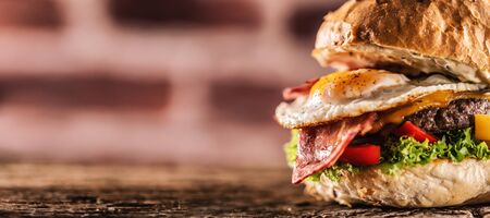 Detail of a burger with beef, cheese, egg, bacon, salad, peppers in a rustic environment.の写真素材