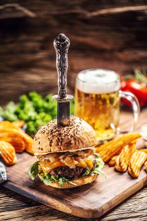Beef burger with caramelized onion and arugula in a rustic wooden environment, a beer and potato wedges on the side.の写真素材