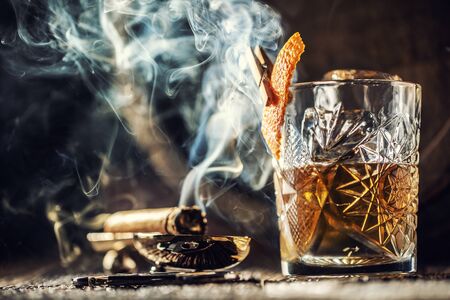 Whisky with no ice in a cup with burning cigar and an old wooden barrel in the background.の写真素材
