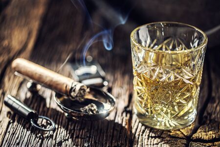 Whisky with no ice in a cup with burning cigar and an old wooden barrel in the background.の写真素材