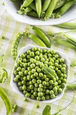 Green raw peas and pods in pocelain bow isolated on wooden table.の写真素材