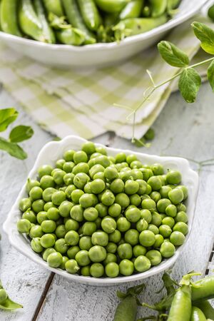 Green raw peas and pods in pocelain bow isolated on wooden table.の写真素材