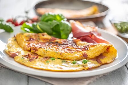 Omelette with prosciutto peas basil tomatoes and herbs on white plate.の写真素材