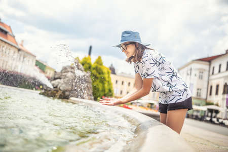 Teenage girl refreshing in a fountain on a hot summer day in the city.の写真素材