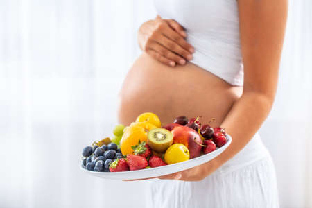 Detail of fruit plate held by a pregnant woman with a white background.の写真素材