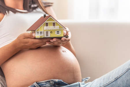Pregnant woman holding a house model in both hands, thinking of taking a real estate mortgage.の写真素材