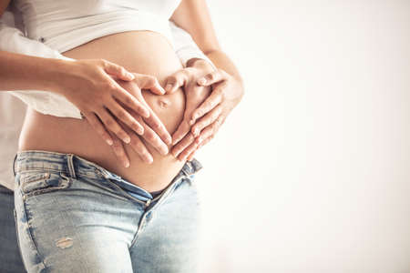 Detail of heart-shaped hands of a couple on a belly of a pregnant woman.