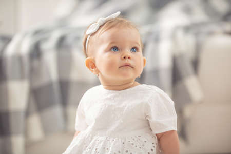 Innocent baby girl looking up with her blue eyes sitting on a floor at home.の写真素材